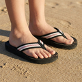 Black flip-flops with white and red baseball stitches worn on a sandy surface