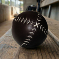 Black leather vintage baseball with white stitching on a wooden baseball dugout bench. 