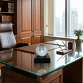 Crystal baseball paperweight on a glass desk in a modern office with wooden cabinets and a cityscape view.