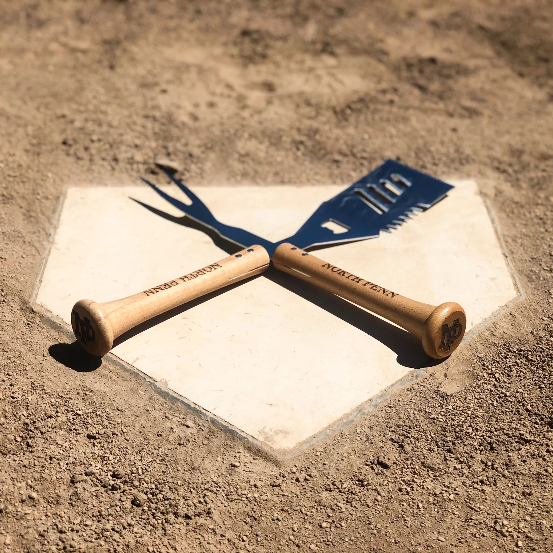 Baseball bat grill tools on a home plate with 'North Penn' branding.