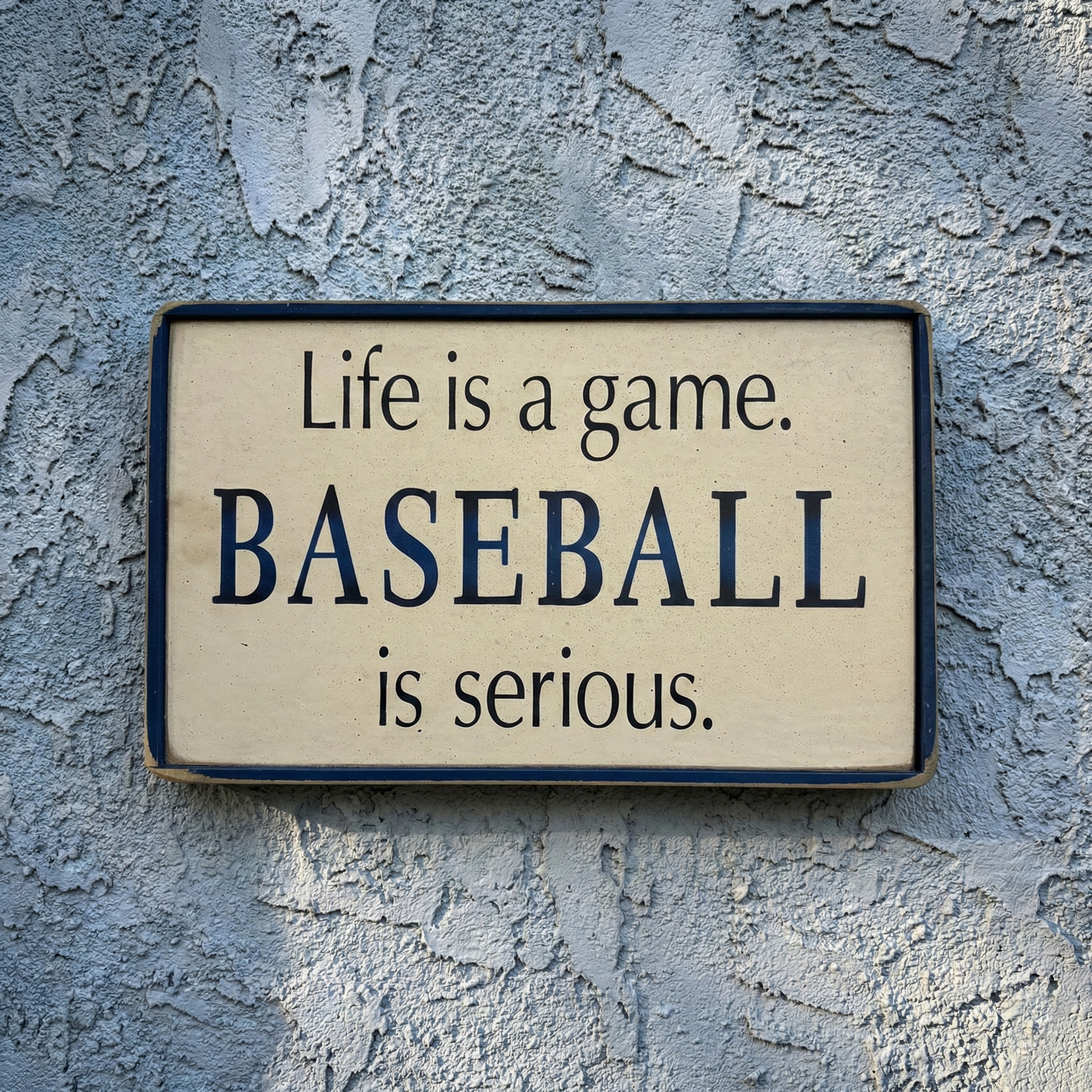 Decorative sign with text 'Life is a game. BASEBALL is serious.' on a textured wall.