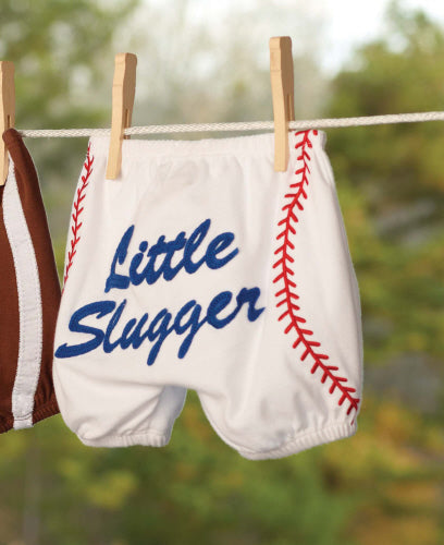 Baby bloomers with 'Little Slugger' text and baseball design on a clothesline.