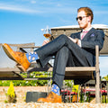 Man in a suit sitting outdoors with a glass of wine, wearing colorful baseball socks.