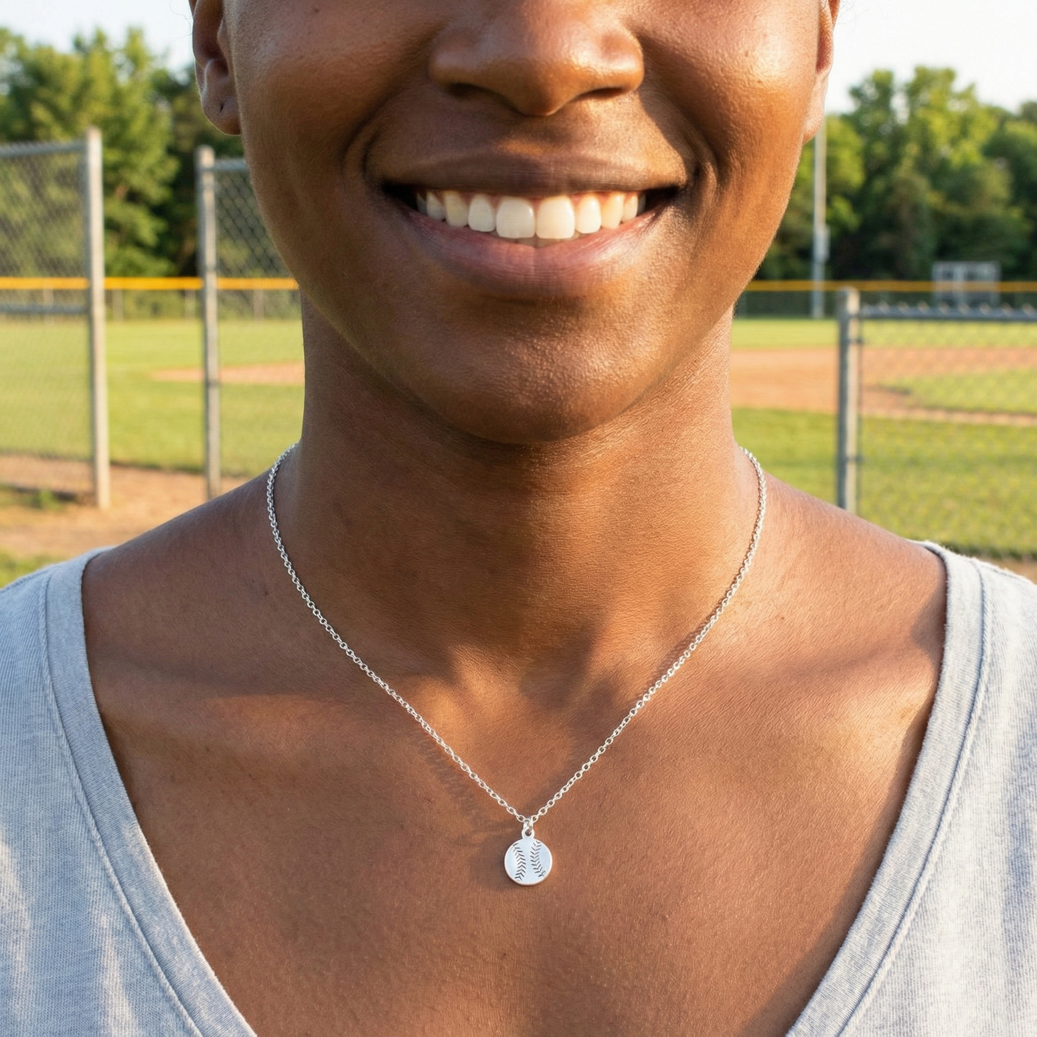 Person wearing a necklace with a silver baseball mini pendant on a sports field background