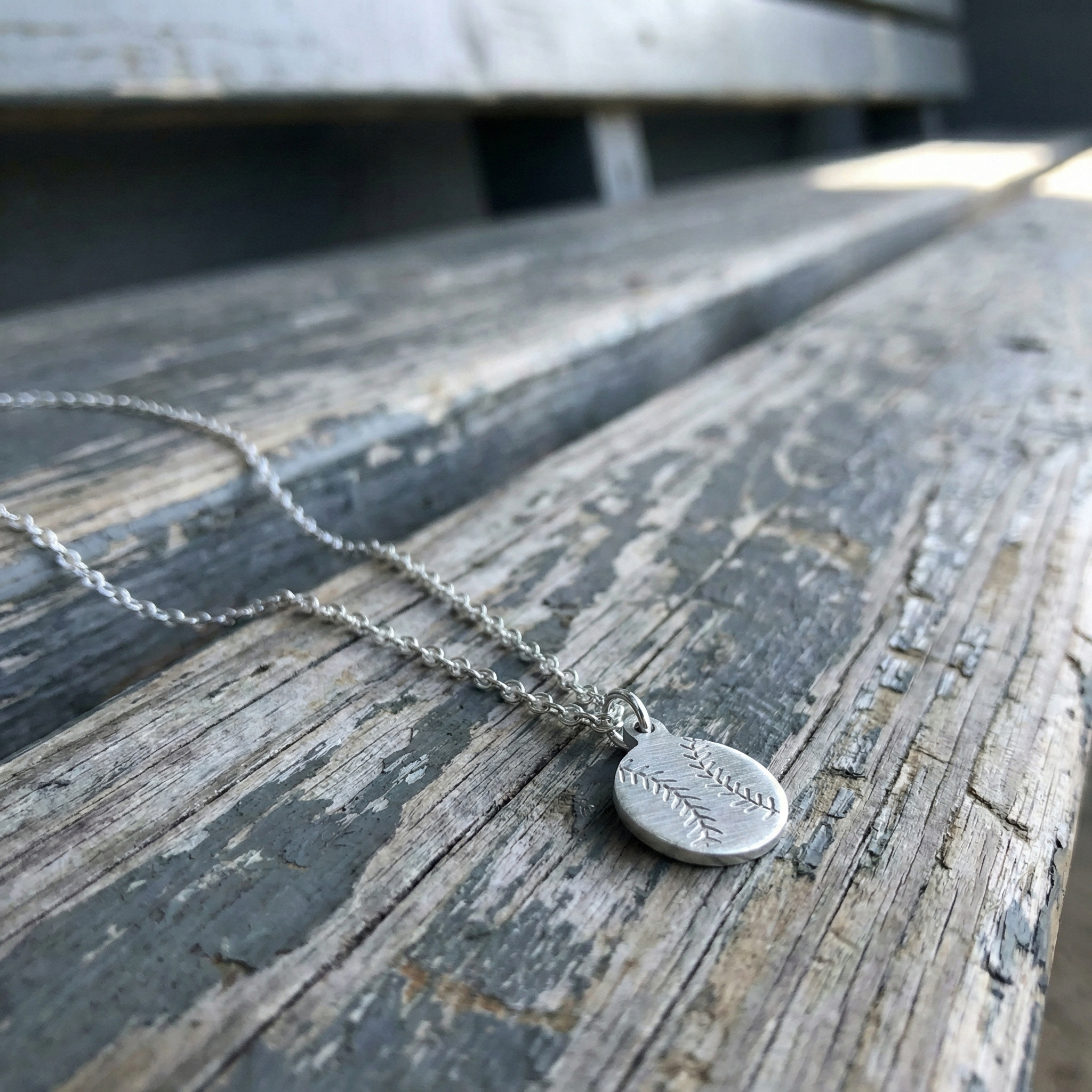 Silver necklace with a mini baseball pendant on a wooden dugout bench