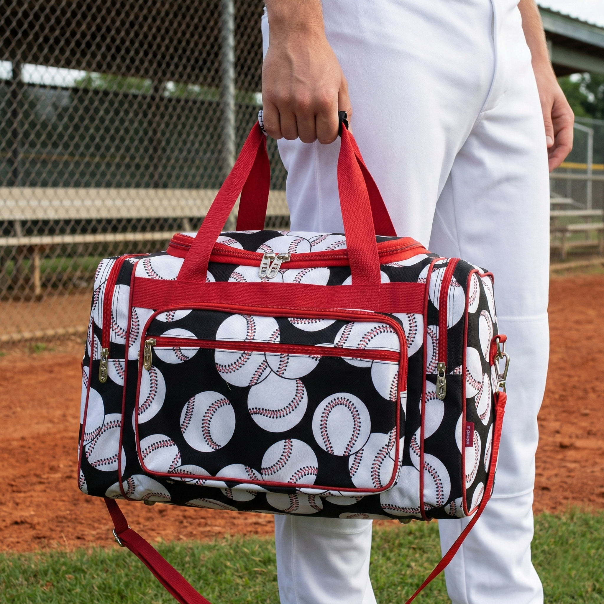 Person holding a duffel bag with baseball pattern on a baseball field