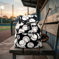 Backpack with baseball pattern on a wooden bench at a baseball field
