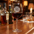 Custom baseball wine glass with 'Smith' engraved on a bar counter with bottles and other glasses.