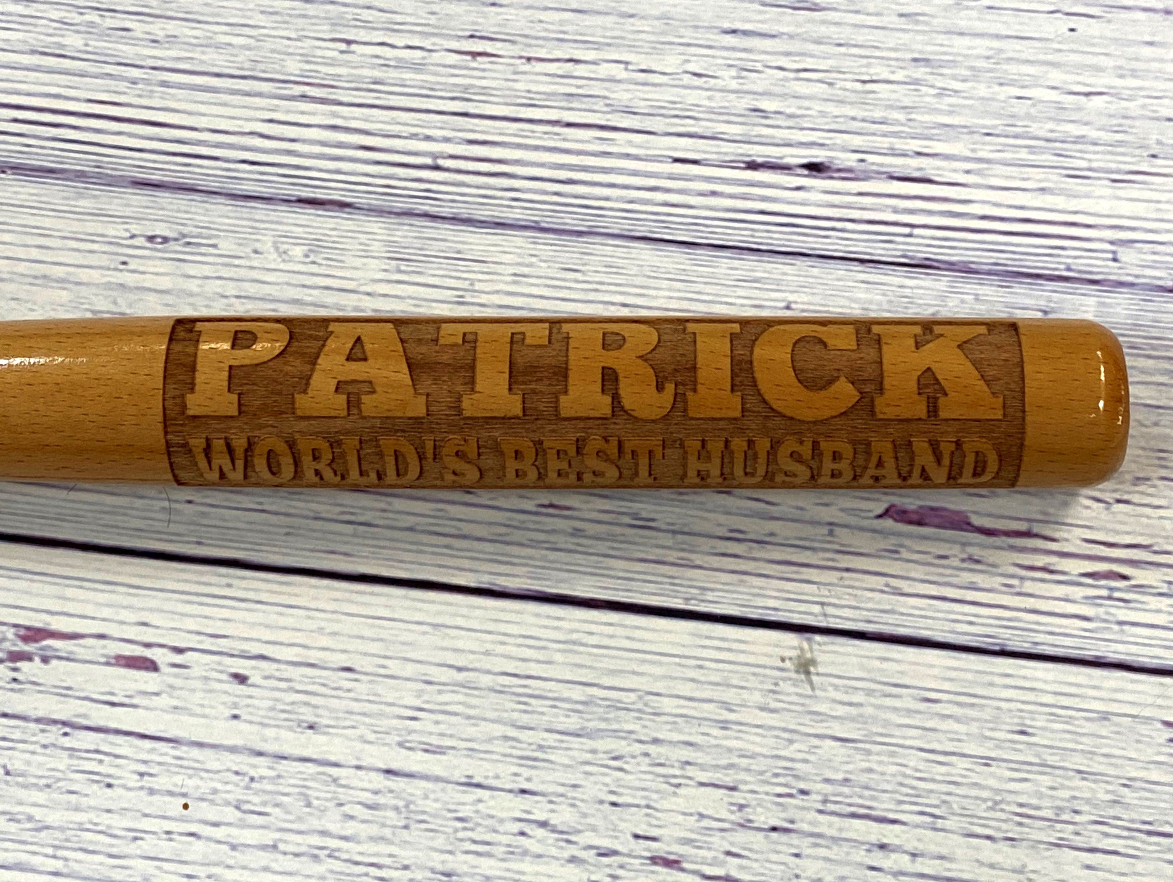 Wooden baseball bat with 'Patrick World's Best Husband' engraving on a textured surface