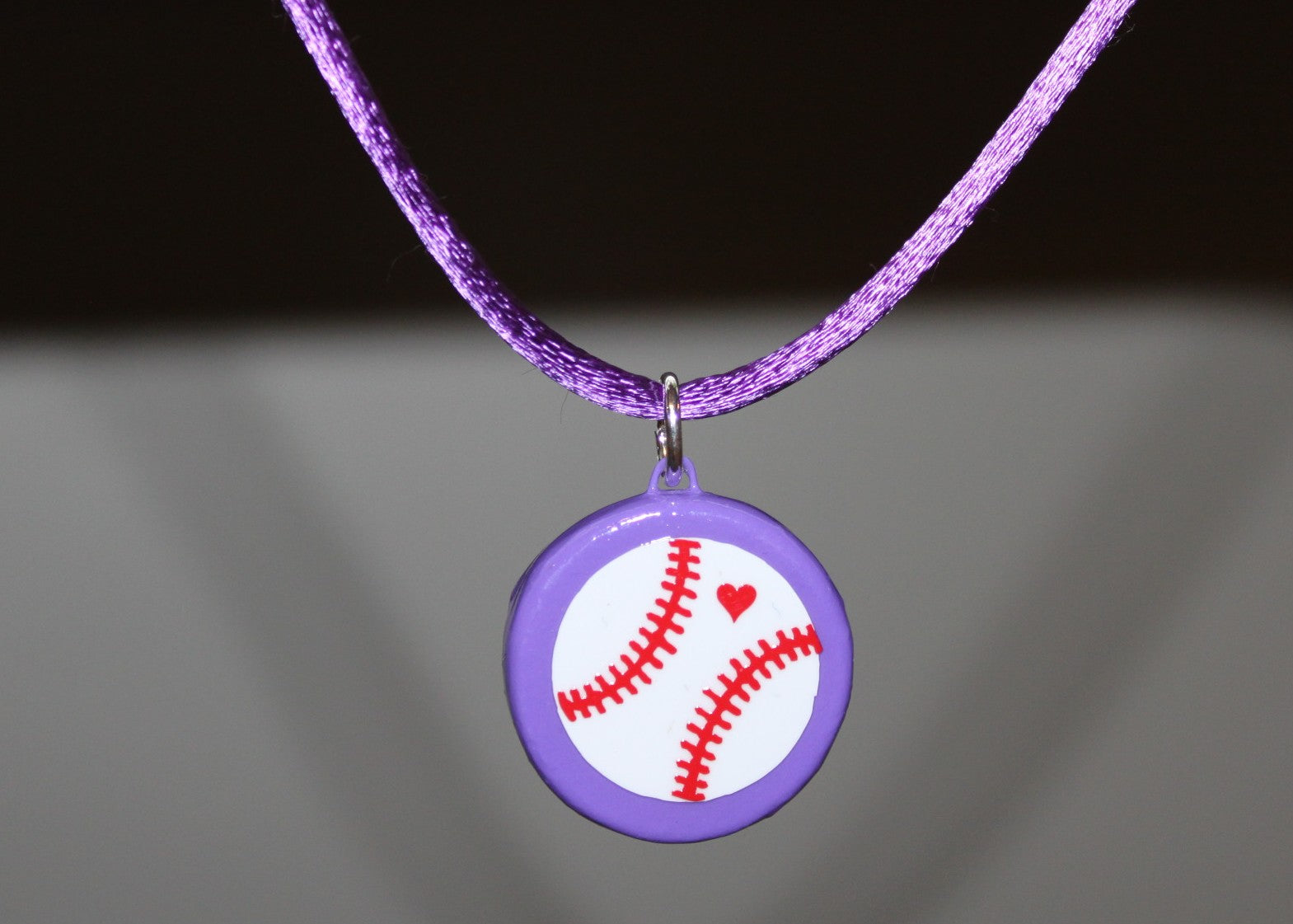 Purple necklace with a baseball pendant on a dark background