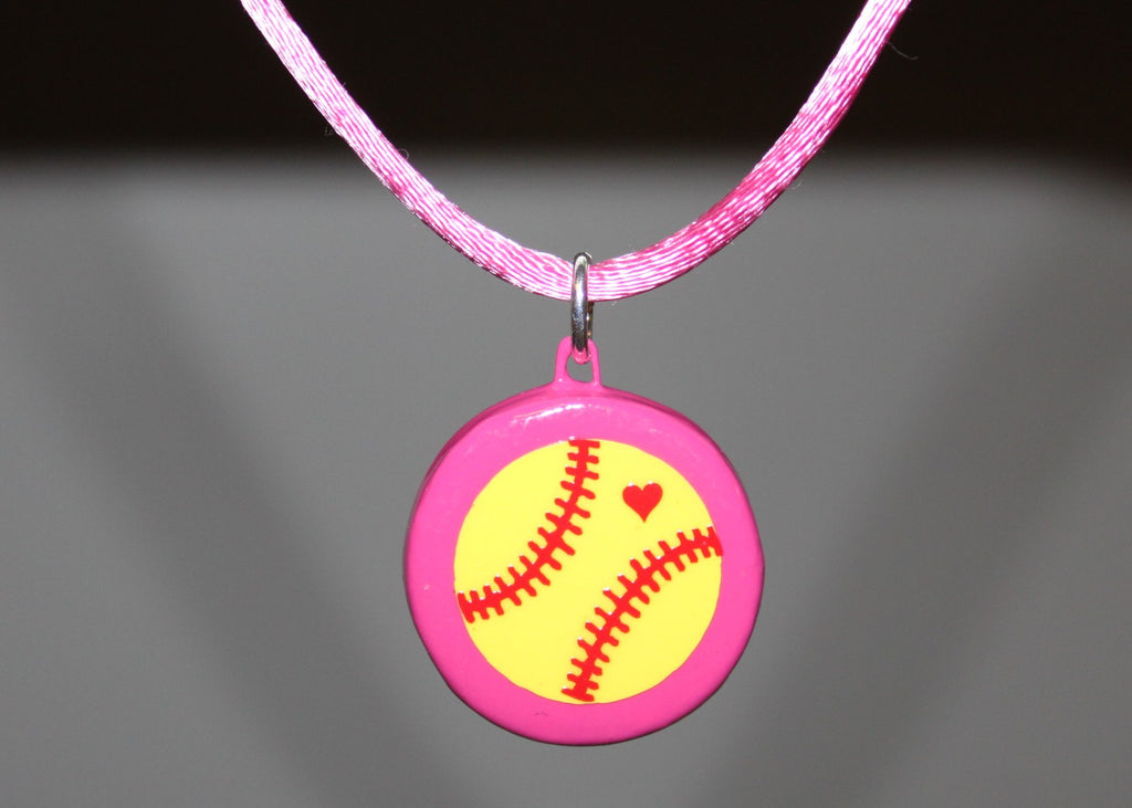 Necklace with a pink and yellow softball pendant on a dark background