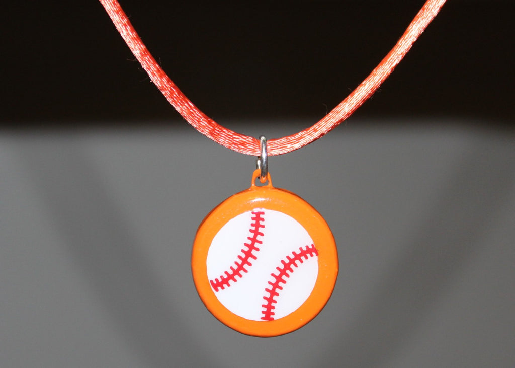 Necklace with a baseball pendant on an orange cord against a dark background
