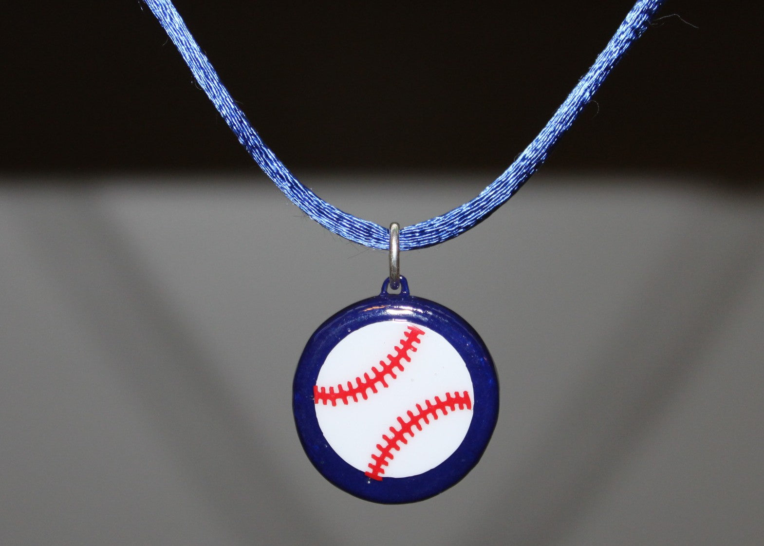Baseball pendant necklace with blue cord on a gray background