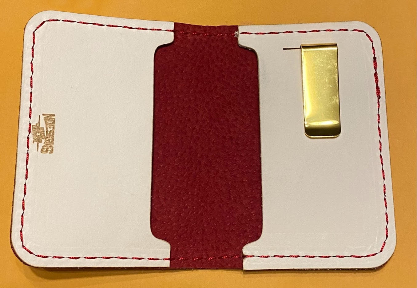 White cardholder leather wallet with red interior and gold clip on a yellow background