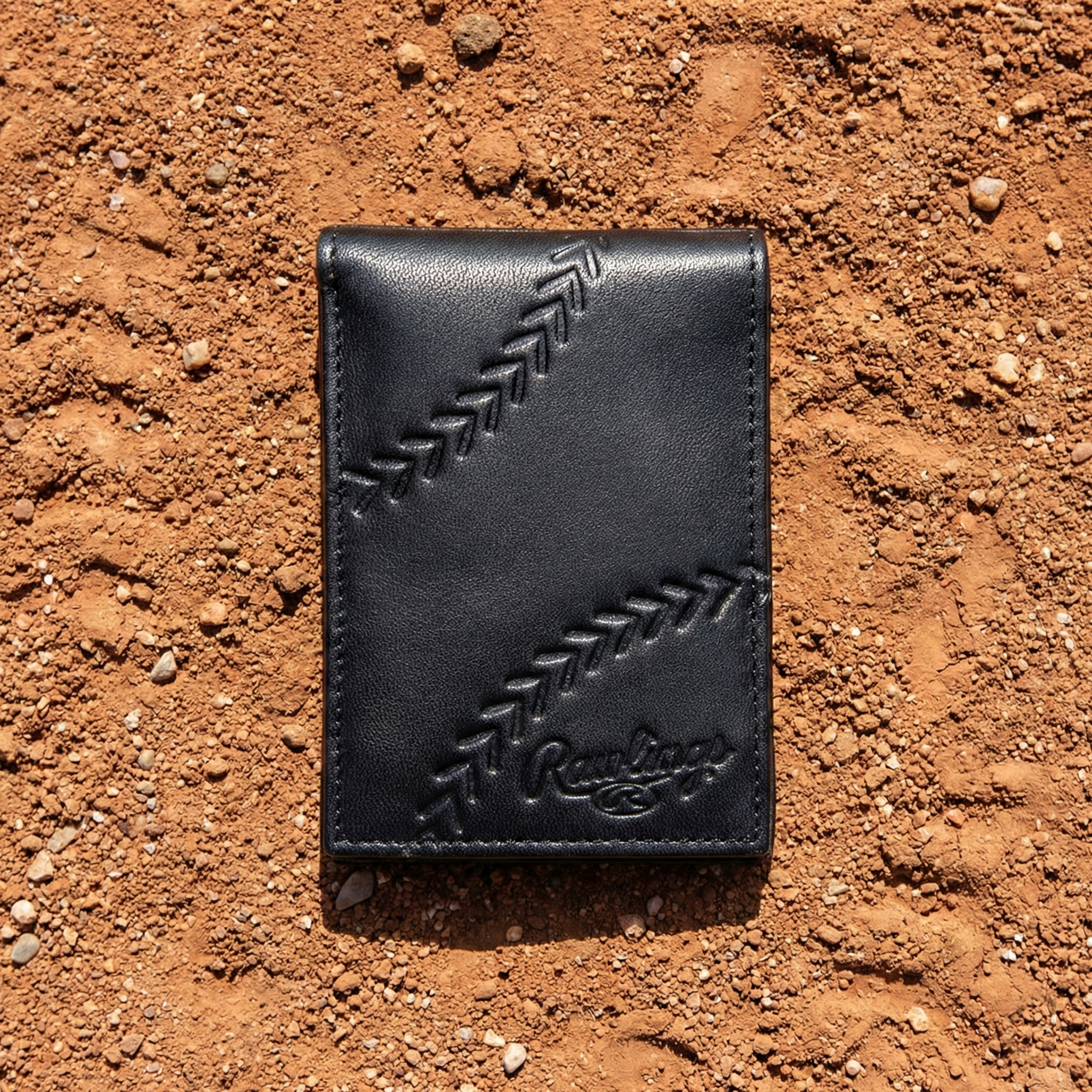 Black leather Rawlings baseball wallet with stitching detail on a dirt surface