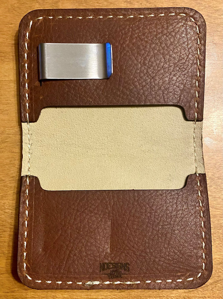 Brown leather money clip with beige interior on a wooden surface