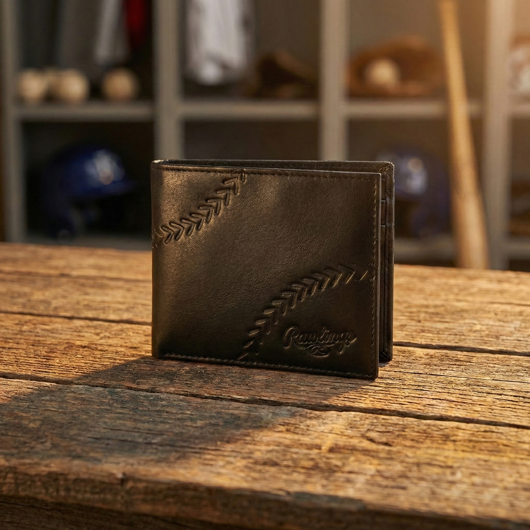 Brown baseball leather wallet with Rawlings embossed logo on a wooden surface, blurred sports equipment in the background