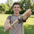 Young boy holding a Rawlings mini baseball bat outdoors with trees in the background