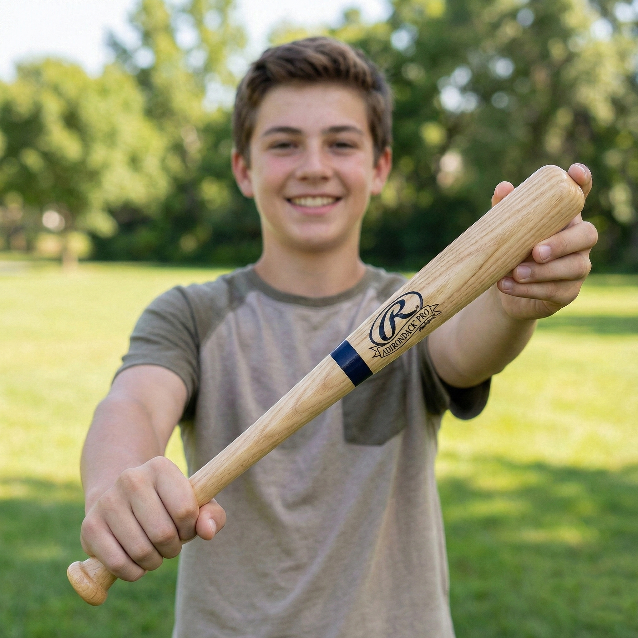 Young boy holding a Rawlings mini baseball bat outdoors with trees in the background