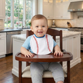 Child sitting in a high chair wearing a bib with a baseball design in a kitchen.