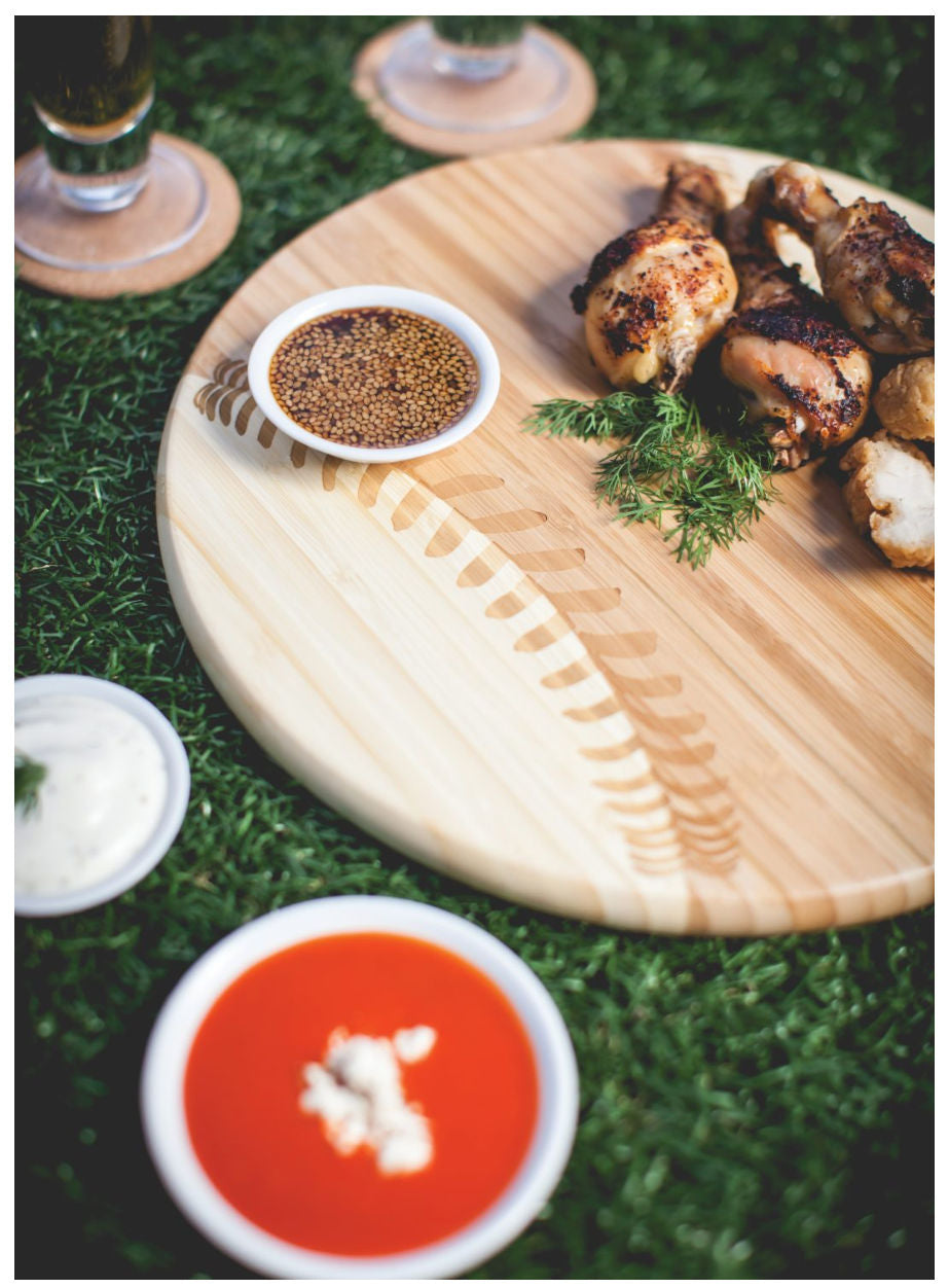 Wooden baseball cutting board with roasted chicken, garnishes, and dips on a grassy background