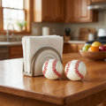 Batter Up Baseball Salt & Pepper Shaker Set on a kitchen counter with a napkin holder and fruit bowl in the background.