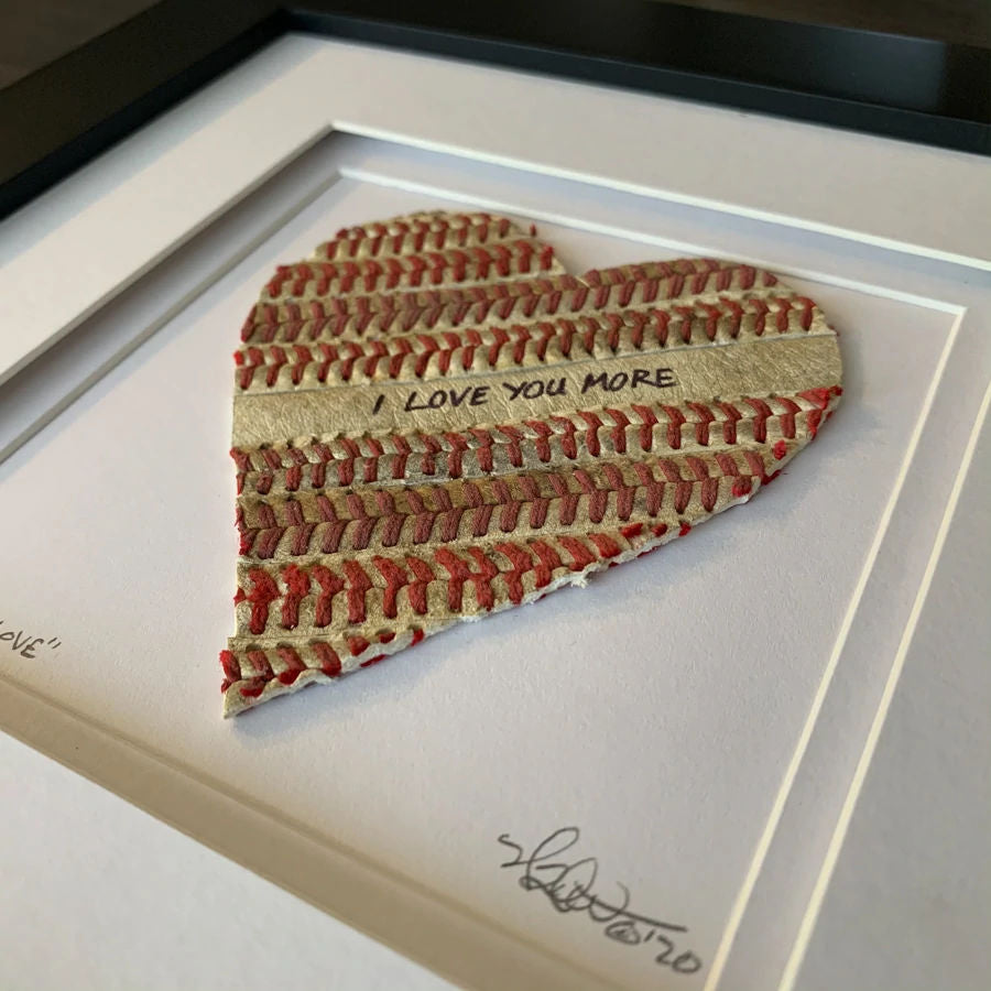Heart-shaped baseball seams artwork with 'I LOVE YOU MORE' text in a framed setting