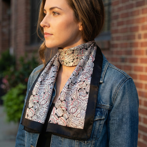 Woman wearing a baseball patterned scarf with a denim jacket against a brick wall.