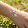 Silver bracelet with a 'I ❤️ Baseball' charm on a wrist against a grassy background