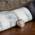 Silver necklace with a baseball-shaped crystal pendant on a textured surface