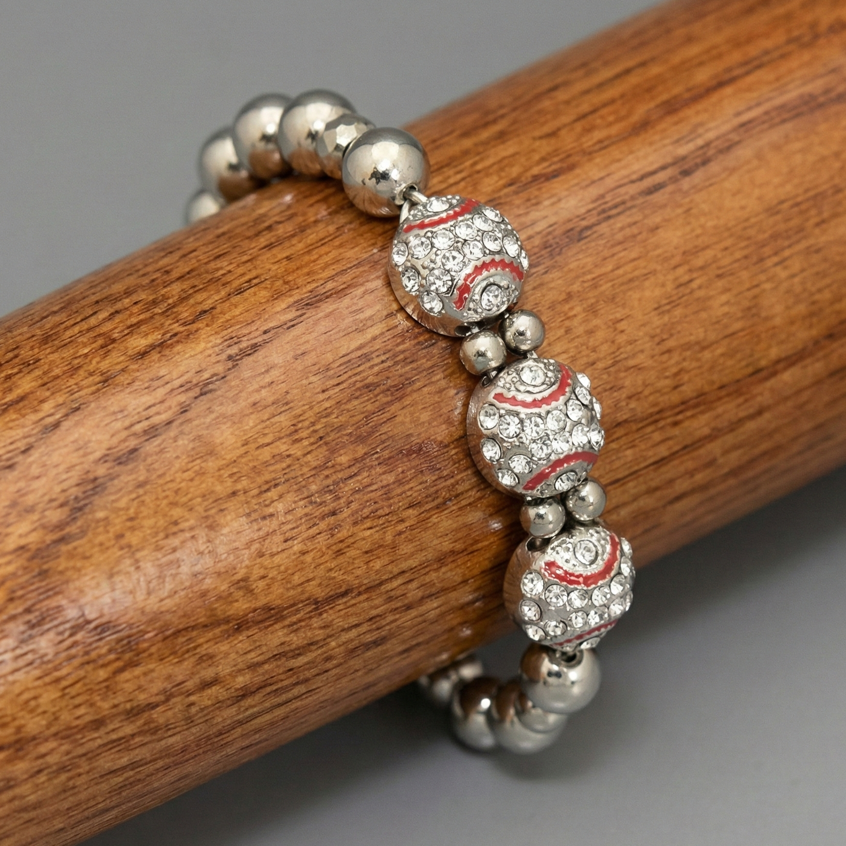 Silver beaded baseball bracelet with red accents on a wooden surface