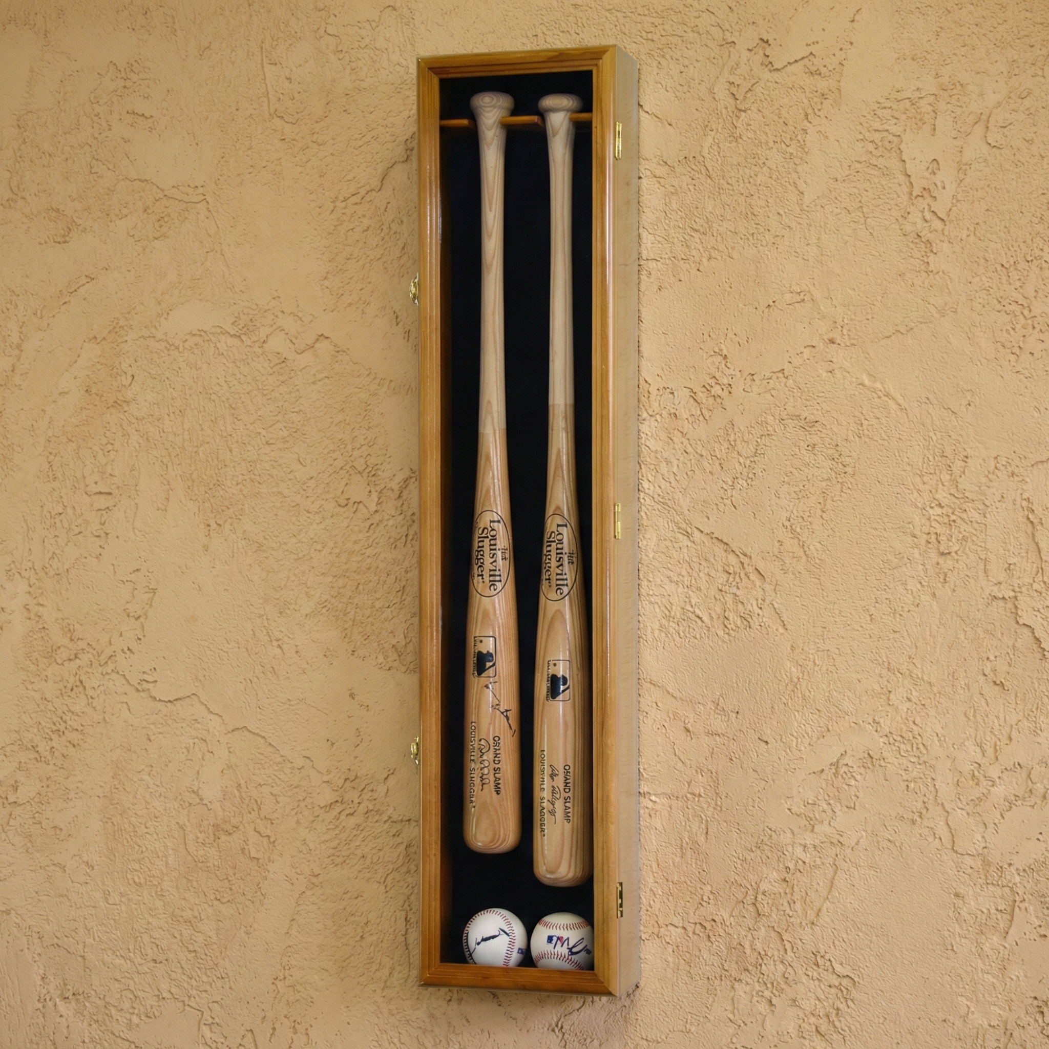 Two baseball bats and two balls in a wooden display case against a beige wall.