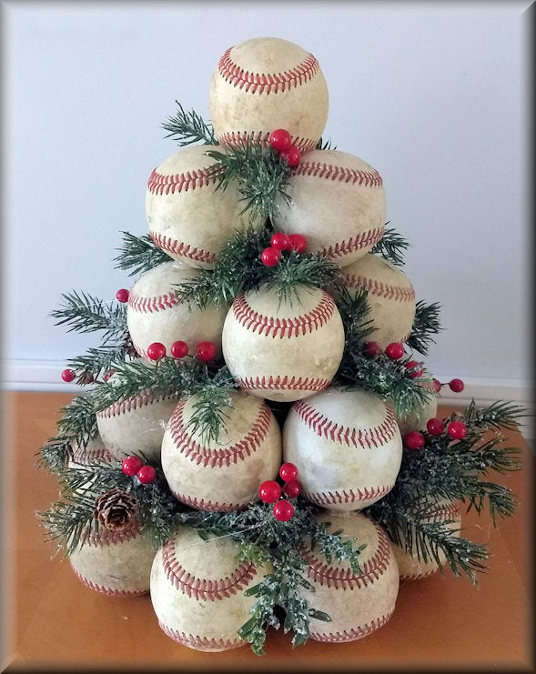 Decorative Christmas tree made of used leather baseballs with greenery and red berries on a white background.