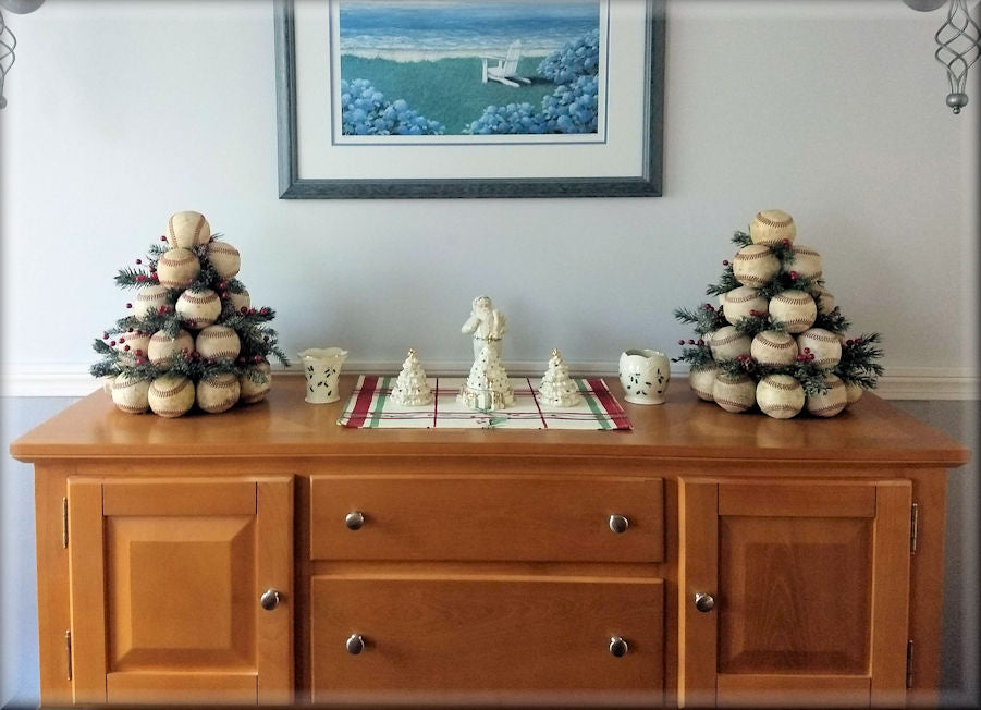 Wooden buffet with decorative items including small baseball Christmas trees and figurines, with a framed picture on the wall.