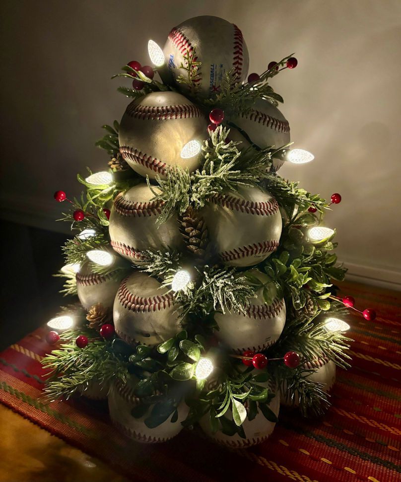 Decorative Christmas tree made of used leather baseballs with lights on a striped surface.