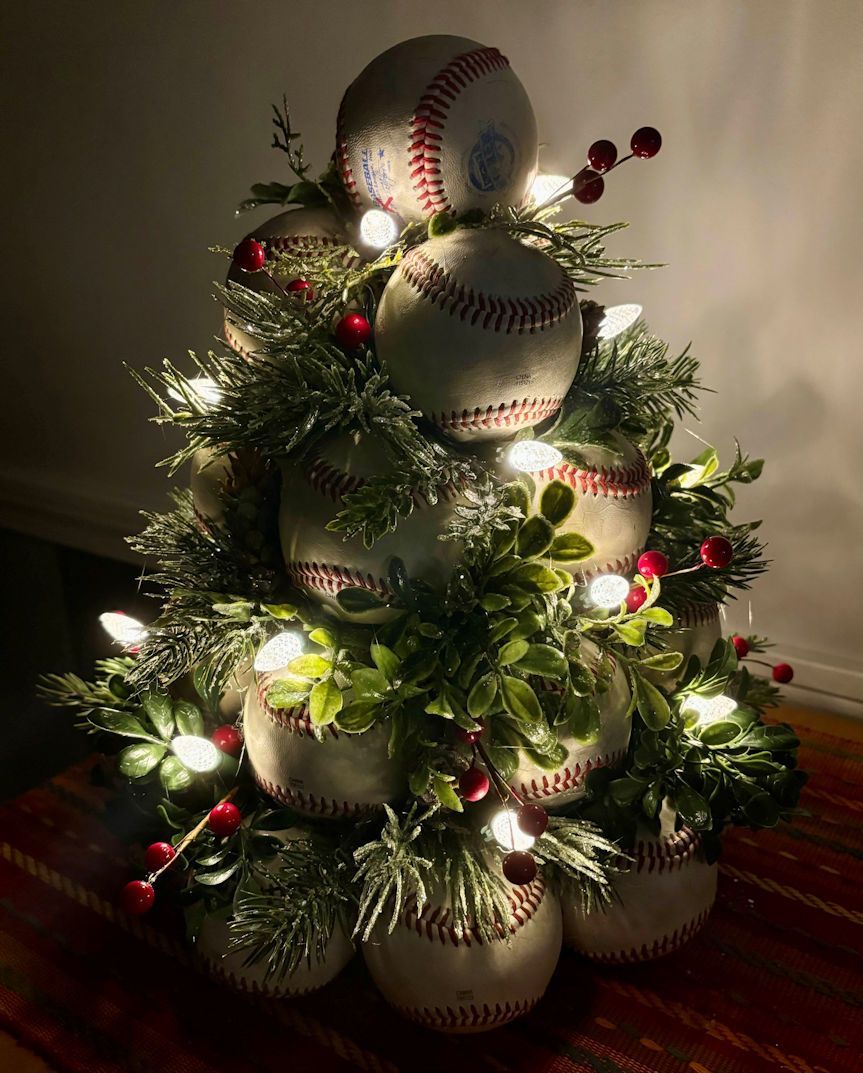 Decorative Christmas tree with lights made of used leather baseballs with greenery on a covered table.