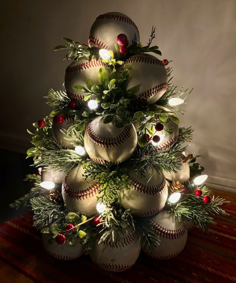 Christmas tree with lights made of used leather baseballs with lights and greenery on a wooden surface.