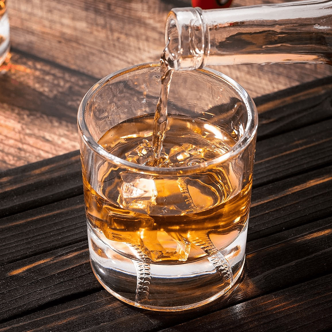 Alcohol being poured into a baseball rocks glass on a wooden surface
