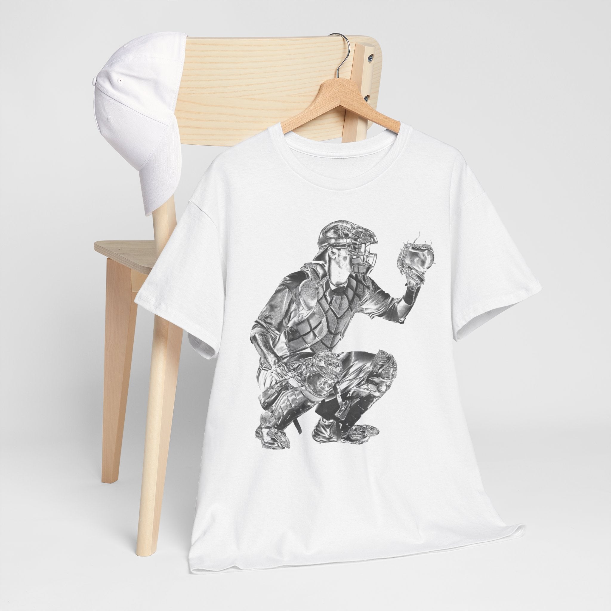 White t-shirt with graphic design of a baseball catcher in gear on a wooden chair.
