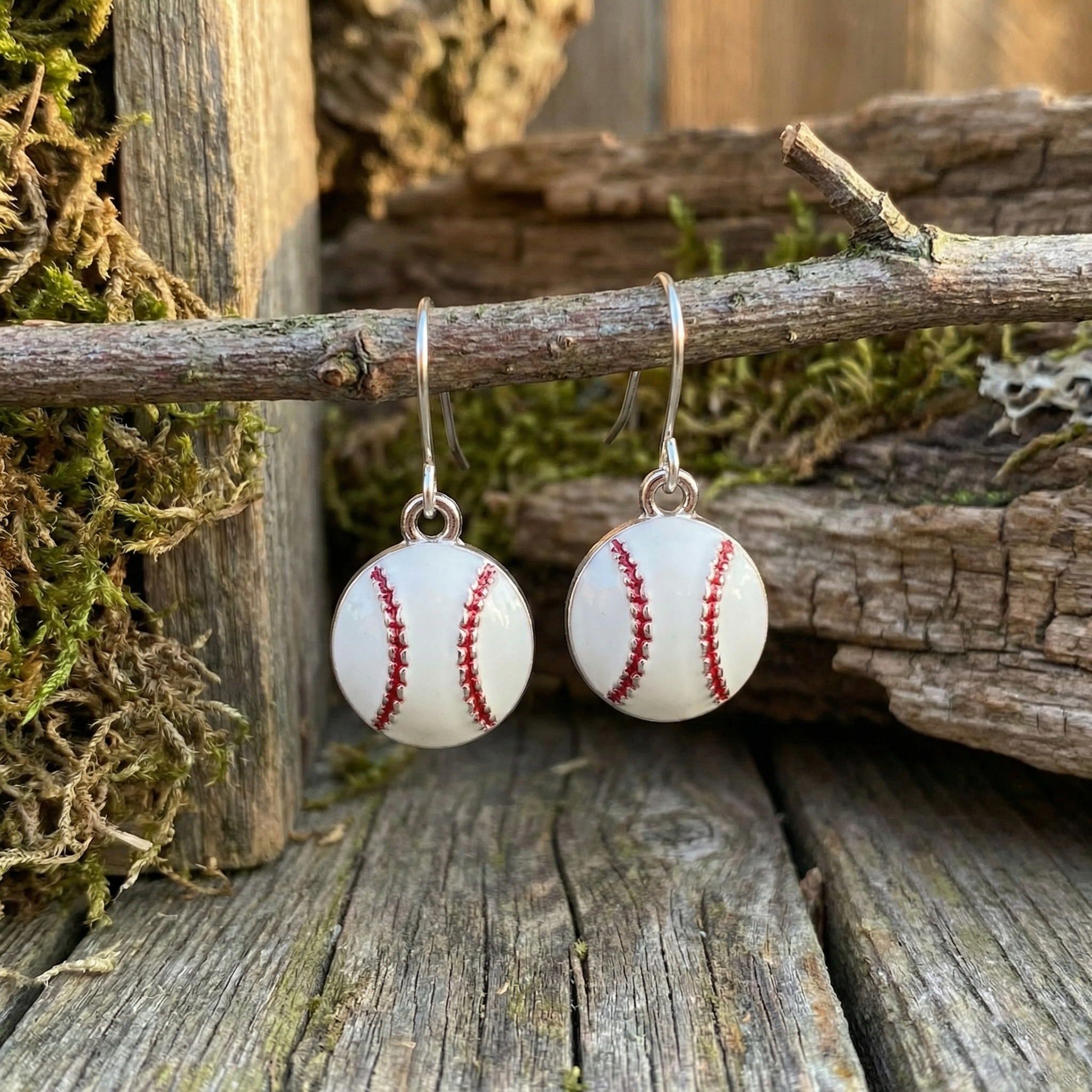 Baseball-shaped dangle hook earrings on a branch with wooden and moss background