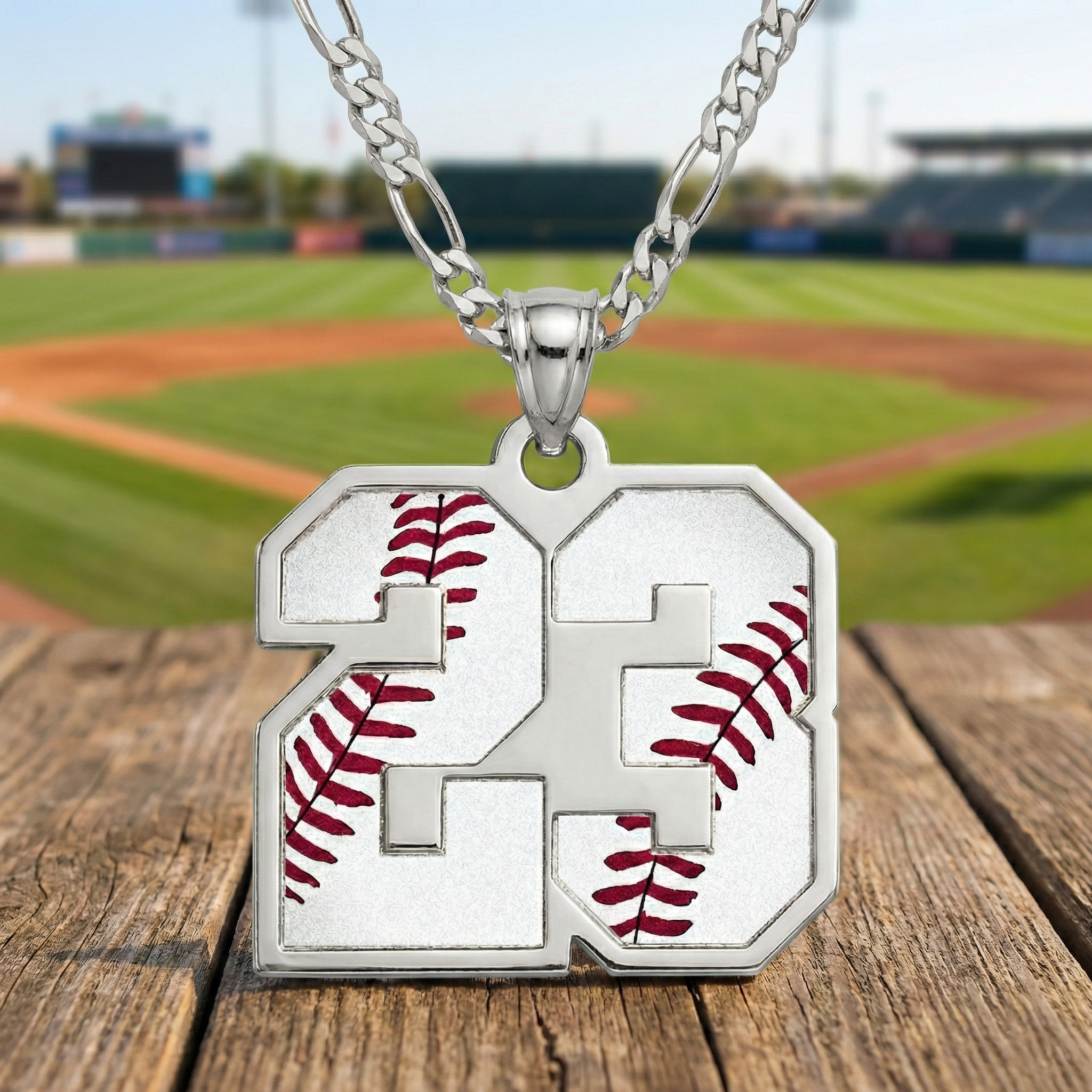 Silver necklace with a pendant featuring the number 23 and baseball design on a wooden surface with a baseball field background.