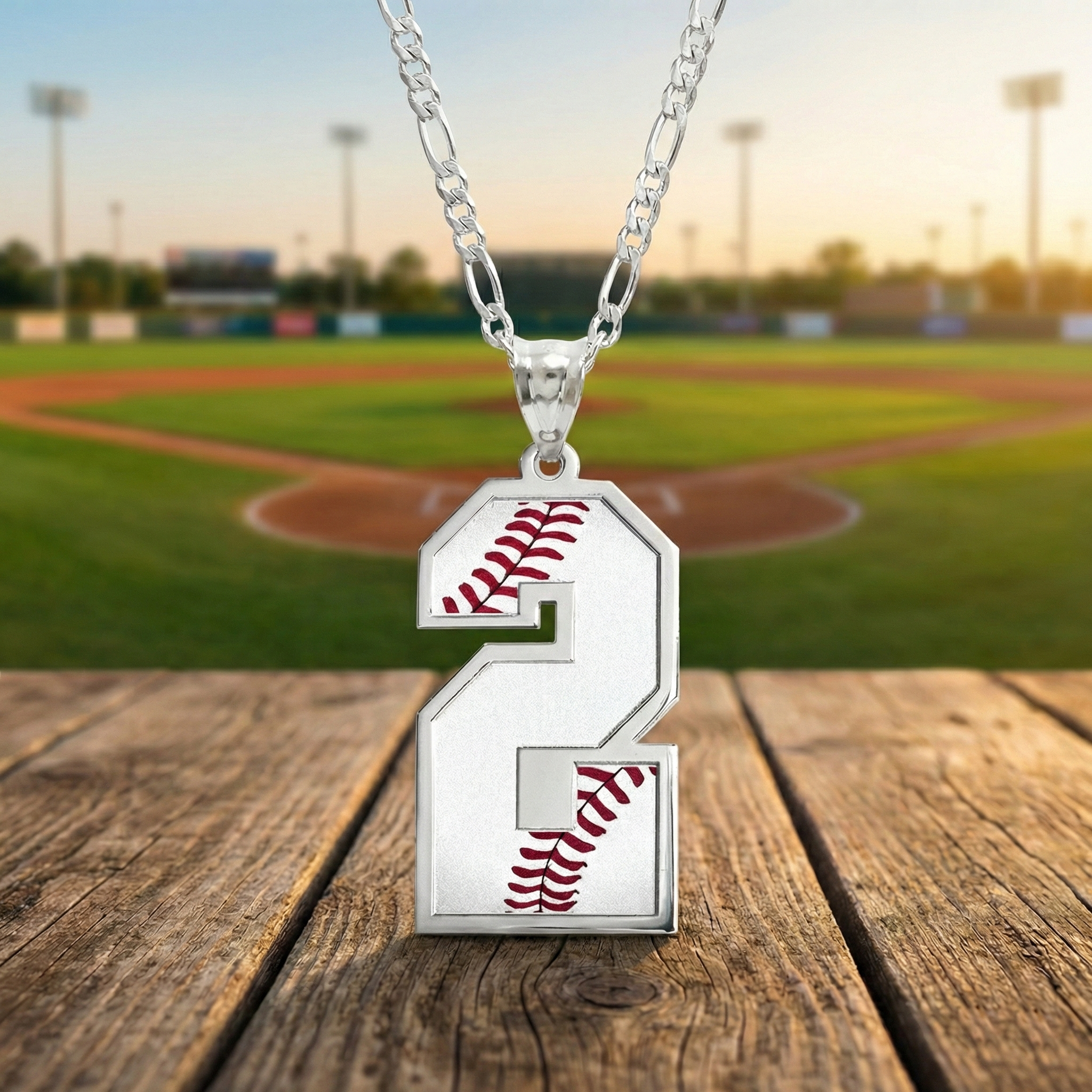 Silver custom necklace with a number 2 baseball pendant on a wooden surface with a baseball field background.